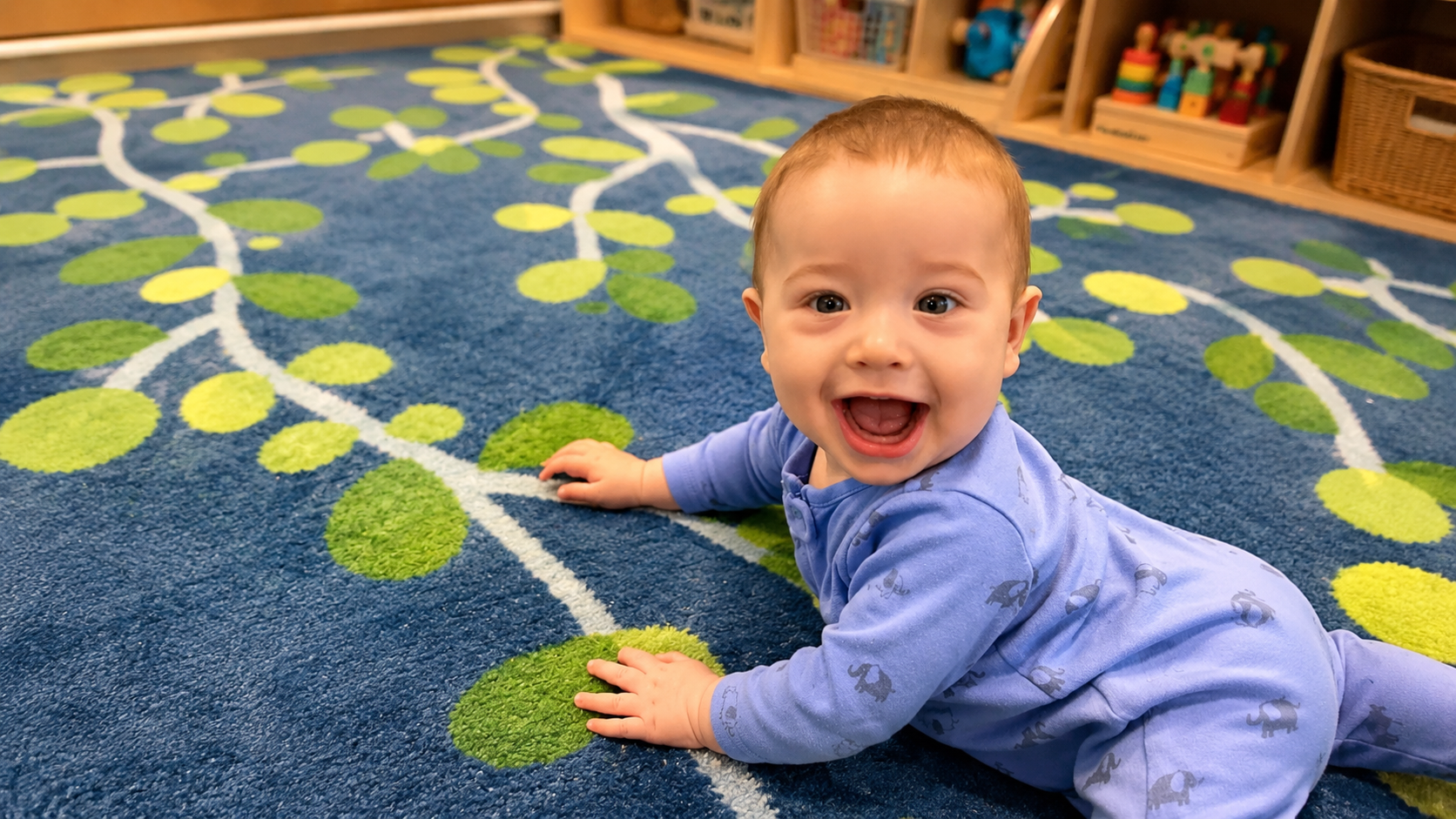 Smiling infant crawling across the leaf-patterned rug in the KinderKids infant room