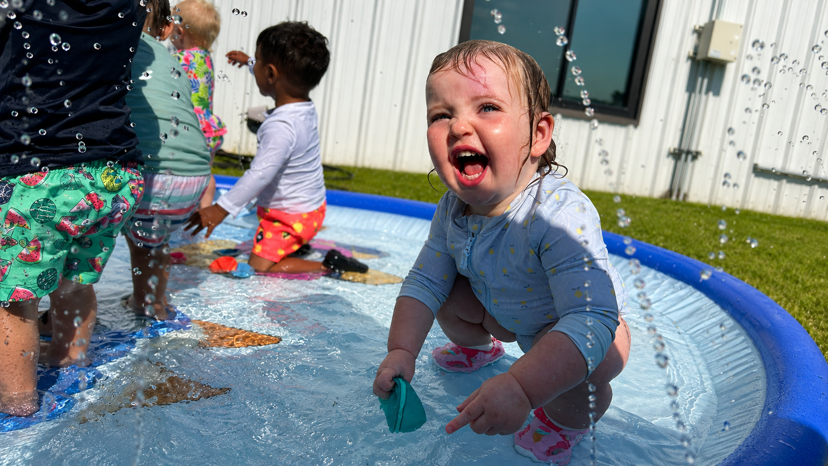 Children laughing and splashing in the outdoor splash pad on a summer afternoon